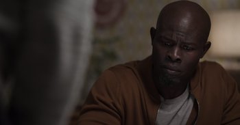 Movie still from “Gran Turismo” (2023), directed by Neill Blomkamp – A man with a beard is sitting down; Close Up shot, Over the shoulder angle