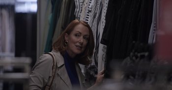 Movie still from “Gran Turismo” (2023), directed by Neill Blomkamp – A woman looking at clothes hanging in a closet; Medium shot, Over the shoulder angle
