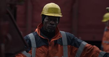 Movie still from “Gran Turismo” (2023), directed by Neill Blomkamp – A construction worker wearing an orange and yellow helmet; Close Up shot, Low angle