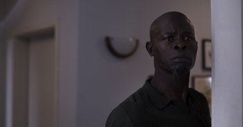 Movie still from “Gran Turismo” (2023), directed by Neill Blomkamp – A man with a black shirt is standing in a room; Close Up shot, Low angle