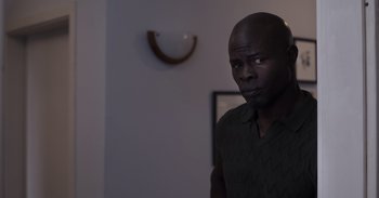 Movie still from “Gran Turismo” (2023), directed by Neill Blomkamp – A man standing in front of a mirror in a room; Medium shot, Over the shoulder angle