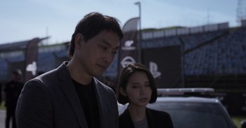 Movie still from “Gran Turismo” (2023), directed by Neill Blomkamp – A man and a woman standing next to each other; Close Up shot, Over the shoulder angle