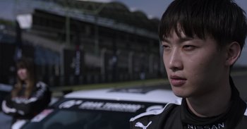 Movie still from “Gran Turismo” (2023), directed by Neill Blomkamp – A young man standing in front of a white car; Close Up shot, Low angle