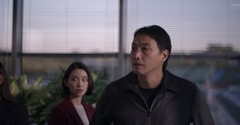 Movie still from “Gran Turismo” (2023), directed by Neill Blomkamp – A man and a woman standing next to each other in front of a window; Medium shot, Over the shoulder angle