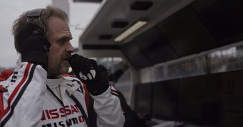 Movie still from “Gran Turismo” (2023), directed by Neill Blomkamp – A man in a white and black jacket talking on a cell phone; Close Up shot, Low angle