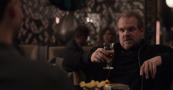 Movie still from “Gran Turismo” (2023), directed by Neill Blomkamp – A man sitting at a table holding a wine glass; Medium shot, Over the shoulder angle