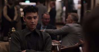 Movie still from “Gran Turismo” (2023), directed by Neill Blomkamp – A man sitting at a table with a drink in front of him; Close Up shot, Over the shoulder angle