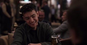 Movie still from “Gran Turismo” (2023), directed by Neill Blomkamp – A man sitting at a table with a glass of beer in front of him; Close Up shot, Over the shoulder angle