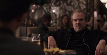 Movie still from “Gran Turismo” (2023), directed by Neill Blomkamp – A man sitting at a table with a glass of beer; Close Up shot, Over the shoulder angle