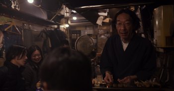 Movie still from “Gran Turismo” (2023), directed by Neill Blomkamp – An older man is cooking food in an asian restaurant; Medium shot, Over the shoulder angle