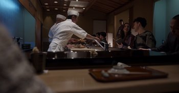 Movie still from “Gran Turismo” (2023), directed by Neill Blomkamp – A group of people are gathered around a table; Medium shot, High angle