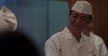 Movie still from “Gran Turismo” (2023), directed by Neill Blomkamp – A man wearing a white chef's hat smiling for the camera; Close Up shot, Low angle