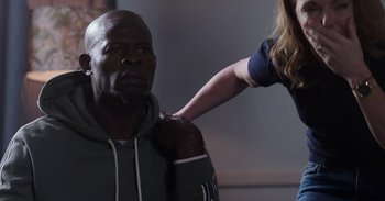 Movie still from “Gran Turismo” (2023), directed by Neill Blomkamp – A woman is helping a man with his hair; Medium shot, Over the shoulder angle