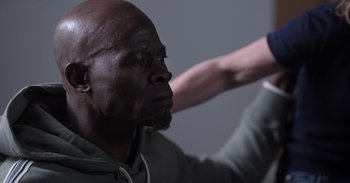 Movie still from “Gran Turismo” (2023), directed by Neill Blomkamp – A man with a beard is looking at something on the wall; Close Up shot, Over the shoulder angle