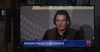 Movie still from “Gran Turismo” (2023), directed by Neill Blomkamp – A man sitting in front of a tv on a news channel; Close Up shot, Over the shoulder angle