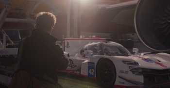Movie still from “Gran Turismo” (2023), directed by Neill Blomkamp – A man is looking at a racing car in the sunlight; Wide shot, Over the shoulder angle