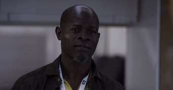 Movie still from “Gran Turismo” (2023), directed by Neill Blomkamp – A man with a beard is wearing a yellow shirt; Close Up shot, Low angle