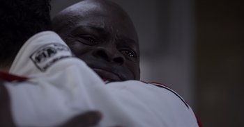 Movie still from “Gran Turismo” (2023), directed by Neill Blomkamp – An older black man holding onto a white pillow; Extreme Close Up shot, Over the shoulder angle