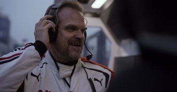 Movie still from “Gran Turismo” (2023), directed by Neill Blomkamp – A man with a beard and glasses is wearing a headset; Close Up shot, Over the shoulder angle