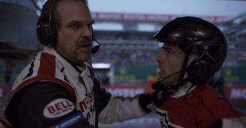 Movie still from “Gran Turismo” (2023), directed by Neill Blomkamp – Two men in racing suits are talking to each other; Close Up shot, Over the shoulder angle