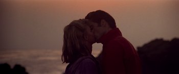 Movie still from “Grease” (1978), directed by Randal Kleiser – A man and a woman kissing in front of the ocean; Medium shot, Low angle