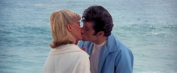 Movie still from “Grease” (1978), directed by Randal Kleiser – A man and a woman kissing near the ocean; Medium shot, Low angle