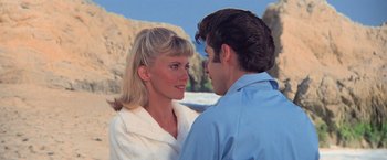 Movie still from “Grease” (1978), directed by Randal Kleiser – A man and a woman standing next to each other on the beach; Medium shot, Over the shoulder angle