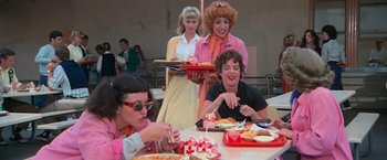 Movie still from “Grease” (1978), directed by Randal Kleiser – A group of women sitting at a table eating food; Medium shot, Over the shoulder angle