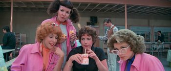 Movie still from “Grease” (1978), directed by Randal Kleiser – A group of people standing around eating food; Medium shot, Low angle