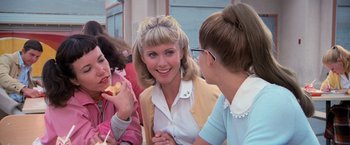 Movie still from “Grease” (1978), directed by Randal Kleiser – A group of people that are eating some food together; Medium shot, Over the shoulder angle