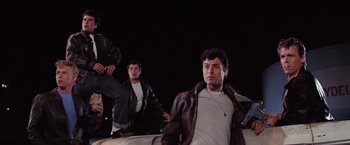 Movie still from “Grease” (1978), directed by Randal Kleiser – A group of young men standing next to each other; Medium shot, Low angle