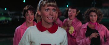 Movie still from “Grease” (1978), directed by Randal Kleiser – A group of young people standing next to each other; Medium shot, Over the shoulder angle
