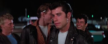 Movie still from “Grease” (1978), directed by Randal Kleiser – A man in a black leather jacket and a man in a brown leather jacket; Close Up shot, Over the shoulder angle