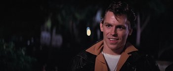 Movie still from “Grease” (1978), directed by Randal Kleiser – A man in a leather jacket smiling for the camera; Close Up shot, Over the shoulder angle