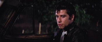 Movie still from “Grease” (1978), directed by Randal Kleiser – A man in a black leather jacket and a white tie; Close Up shot, Over the shoulder angle