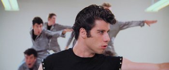 Movie still from “Grease” (1978), directed by Randal Kleiser – A man with a black shirt is looking to his left; Medium shot, Low angle