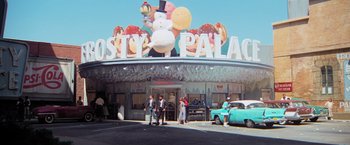 Movie still from “Grease” (1978), directed by Randal Kleiser – People are standing in front of a restaurant; Extreme Wide shot, Low angle