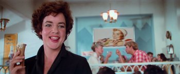 Movie still from “Grease” (1978), directed by Randal Kleiser – A woman in a black shirt is in a restaurant; Close Up shot, Over the shoulder angle