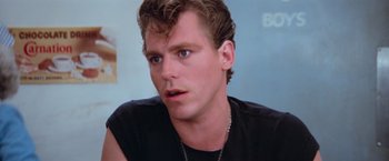 Movie still from “Grease” (1978), directed by Randal Kleiser – A person wearing a black t - shirt; Close Up shot, Over the shoulder angle