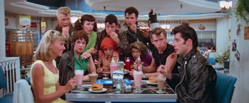 Movie still from “Grease” (1978), directed by Randal Kleiser – A group of people sitting around a table eating; Wide shot, High angle
