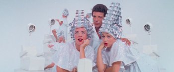 Movie still from “Grease” (1978), directed by Randal Kleiser – A group of people with hair dryers on their heads; Medium shot, Low angle