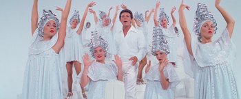 Movie still from “Grease” (1978), directed by Randal Kleiser – A group of people in white outfits and silver wigs; Medium shot, Low angle