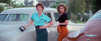 Movie still from “Grease” (1978), directed by Randal Kleiser – Two women standing in front of a white car; Medium shot, Low angle