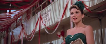 Movie still from “Grease” (1978), directed by Randal Kleiser – A woman standing in front of a building wearing a green dress; Medium shot, Low angle