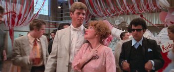 Movie still from “Grease” (1978), directed by Randal Kleiser – A man and a woman in formal wear standing next to each other; Close Up shot, Over the shoulder angle