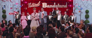 Movie still from “Grease” (1978), directed by Randal Kleiser – A group of people in formal wear performing on a stage; Wide shot, High angle