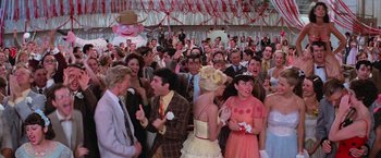 Movie still from “Grease” (1978), directed by Randal Kleiser – A group of people standing around each other at an event; Wide shot, High angle
