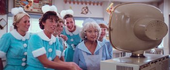 Movie still from “Grease” (1978), directed by Randal Kleiser – A group of women standing in front of a mirror in a room; Medium shot, Over the shoulder angle
