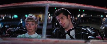 Movie still from “Grease” (1978), directed by Randal Kleiser – A man and a woman sitting in the back of a car; Medium shot, Over the shoulder angle
