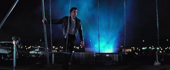 Movie still from “Grease” (1978), directed by Randal Kleiser – A man in a leather jacket standing on a swing; Wide shot, Low angle